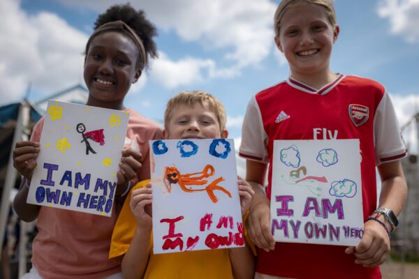 three children holding hand painted signs saying I am my own hero at camp mirage