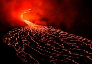 Spectacular lava flow from an erupting volcano under the night sky, showcasing fiery reds and intense heat.